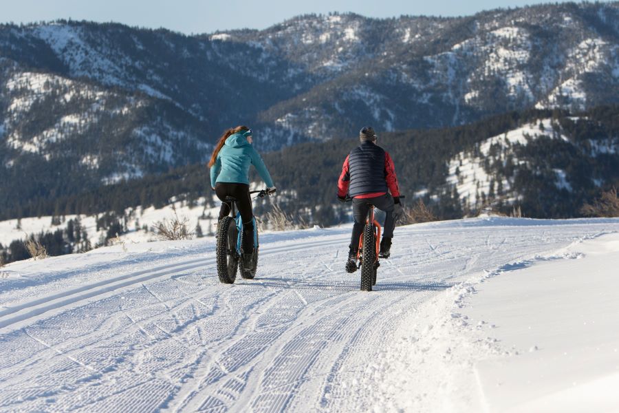 Two riders on fat bikes going down a snowy path